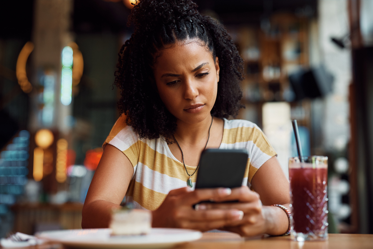 Woman sitting alone at a café looking at her phone with a concerned expression, representing friendship breakups and outgrowing friends.