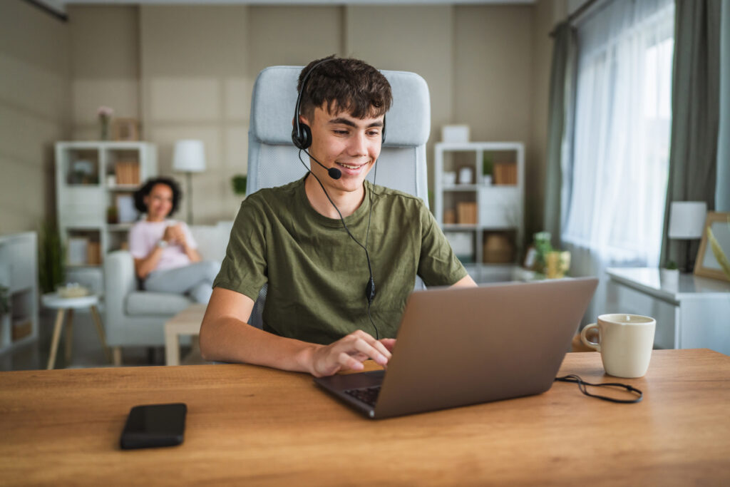 Teen wearing a headset smiling while playing video games and talking with friends online