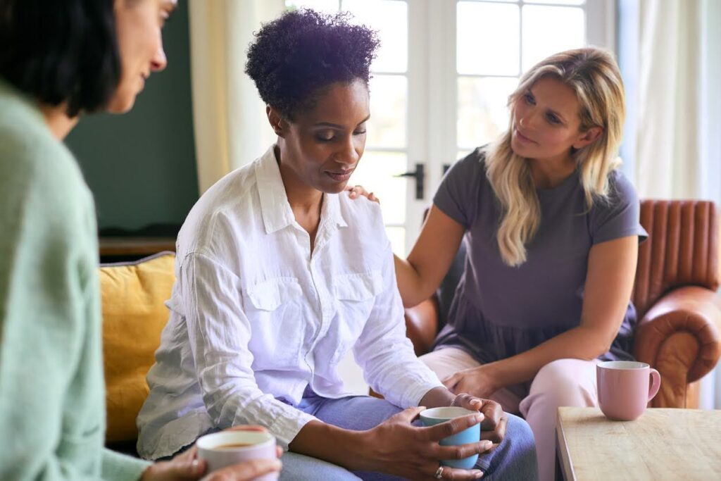 Three women sitting together indoors during a quiet, supportive moment