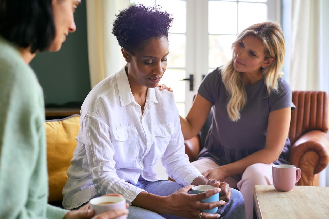 Three women sitting together indoors during a quiet, supportive moment