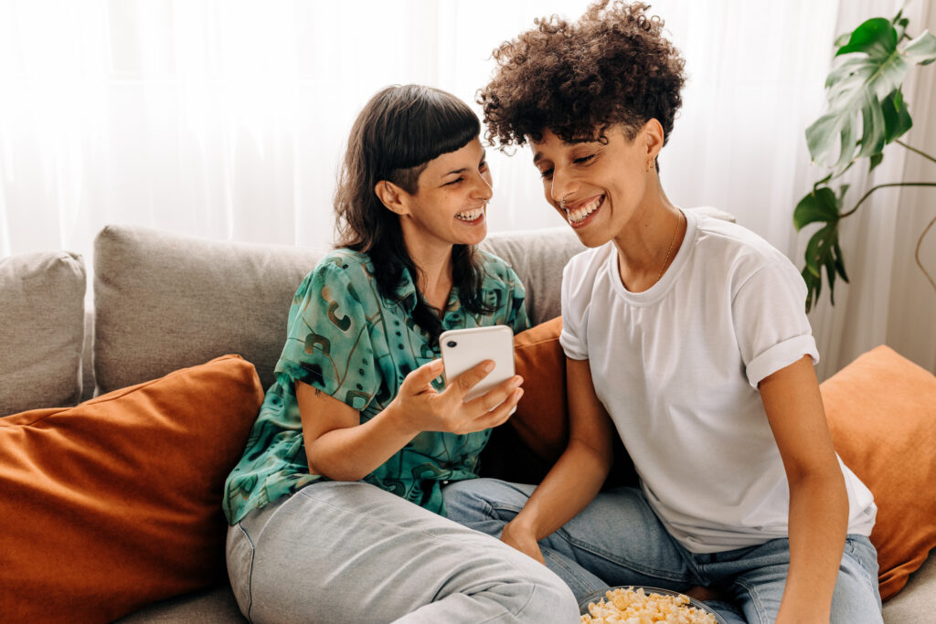 Two lesbian lovers using a smartphone together at home. Lesbian couple smiling cheerfully