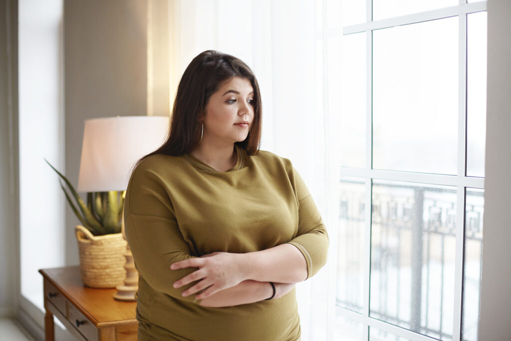 Women standing at a window, looking out and thinking