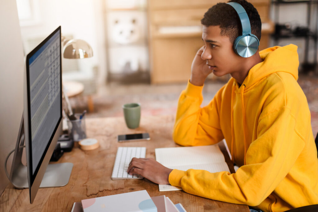 Male teen taking an assessment with headphones on sitting at a computer